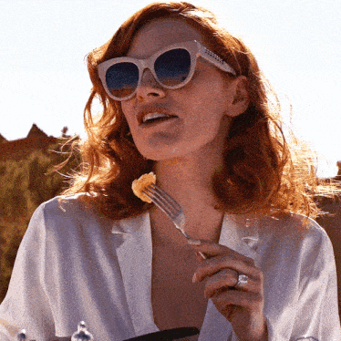 a woman wearing sunglasses holds a fork in her mouth