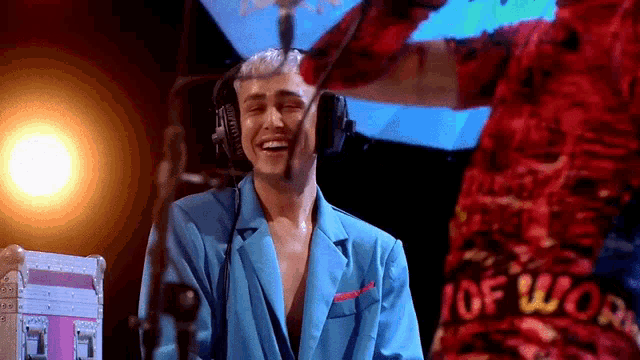 a man wearing headphones is laughing while another man in a red shirt stands behind him with the word worn on it