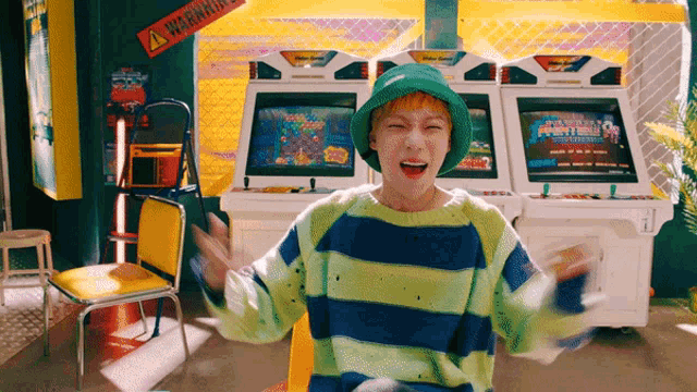 a man wearing a green hat and a striped sweater stands in front of an arcade machine with a warning sign above it