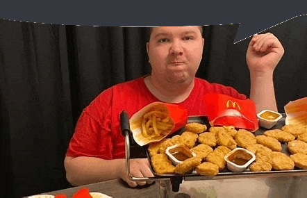 a man is sitting at a table eating nuggets and french fries from a mcdonald 's tray .
