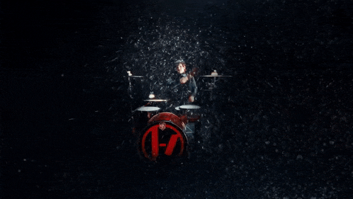 a man playing drums in a dark room with lights behind him