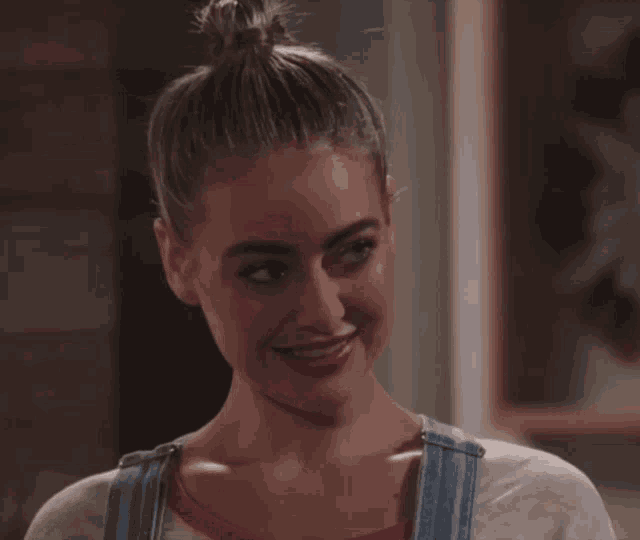 a woman wearing overalls and a bun is smiling