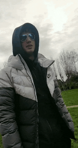a man wearing sunglasses and a nike jacket is standing in a field