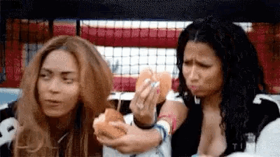 two women are sitting next to each other eating hot dogs and making funny faces .