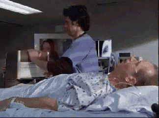a man in a hospital gown is laying on a bed with a nurse standing behind him