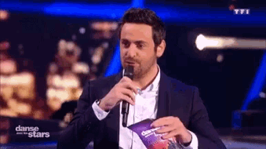 a man in a suit is singing into a microphone while holding a booklet .