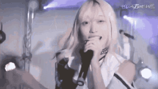 a girl with blonde hair is singing into a microphone on a stage