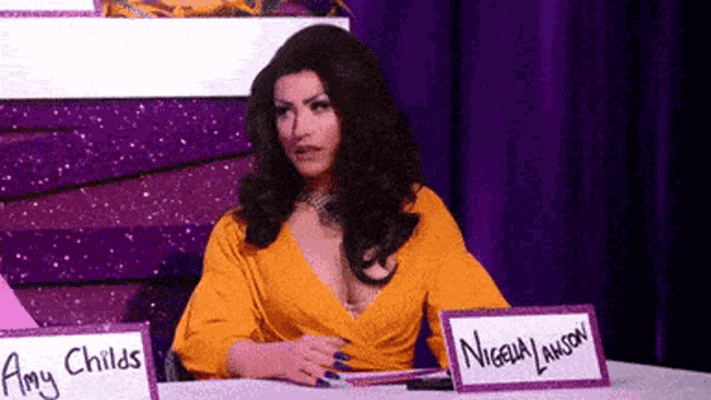 a woman in a yellow dress is sitting at a table with a name tag that says amy childs