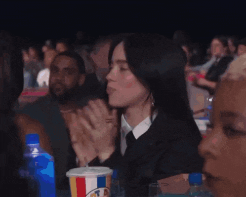 a woman applauds while sitting in a crowd with a cup of mcdonald 's soda