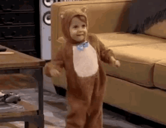 a toddler in a teddy bear costume is dancing in a living room .