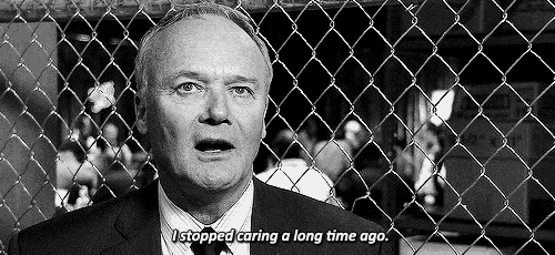 a man in a suit and tie is standing behind a chain link fence and talking .