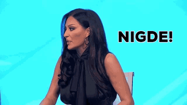 a woman in a black dress is sitting in front of a blue background with the word nigde written on it .