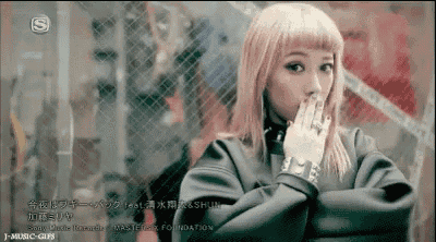 a woman with pink hair is covering her mouth with her hand while wearing a black jacket