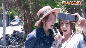 a woman wearing a straw hat is taking a picture of another woman with a cell phone .