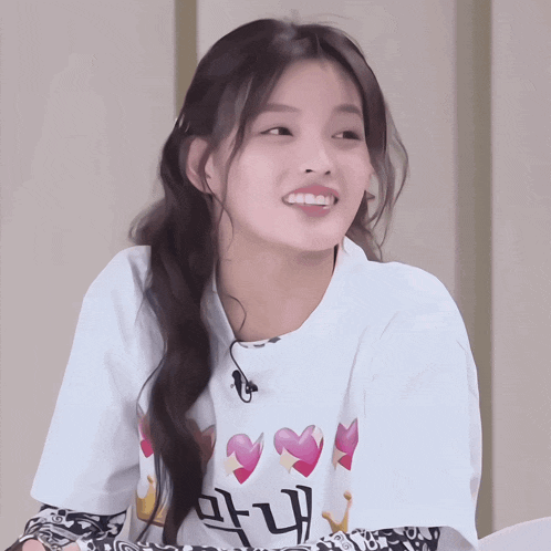 a woman wearing a white t-shirt with hearts and crowns on it is smiling