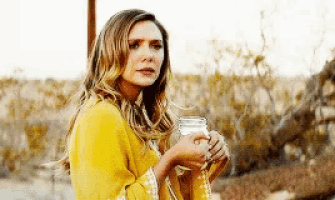 a woman in a yellow sweater is holding a mason jar of milk .