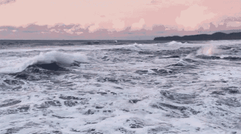a large body of water with waves crashing on the shore at sunset