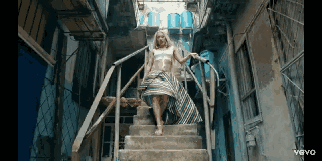 a woman in a striped skirt is walking up a set of stairs with the word vevo on the bottom