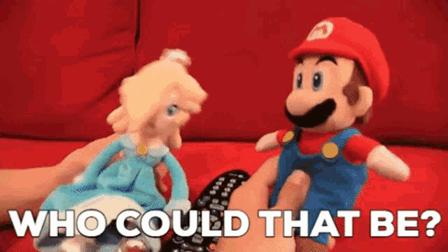 a person holding a remote control next to a stuffed mario and princess peach