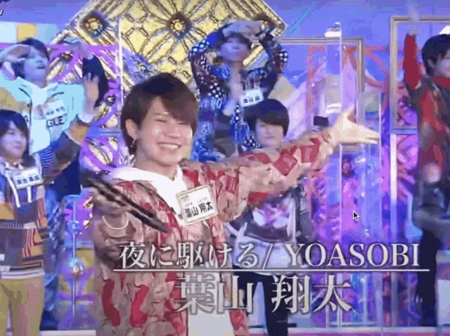 a group of people standing in front of a sign that says yoasobi on it