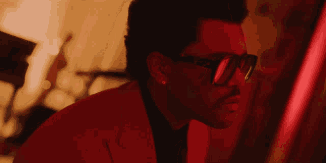a man wearing glasses and a red suit looks to the side