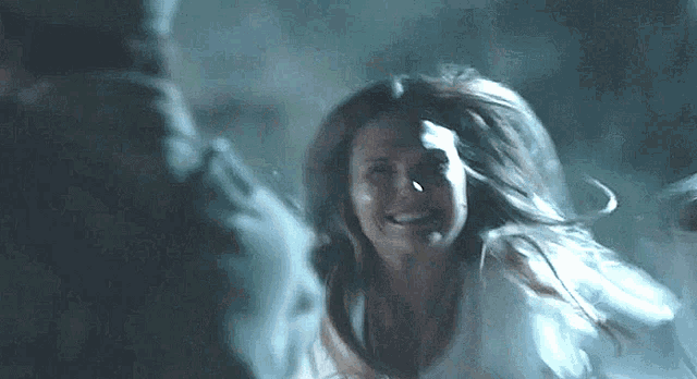 a woman in a white shirt is running in a dark room with her hair blowing in the wind .