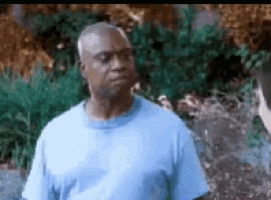 a man in a blue shirt is standing in front of a lush green forest .