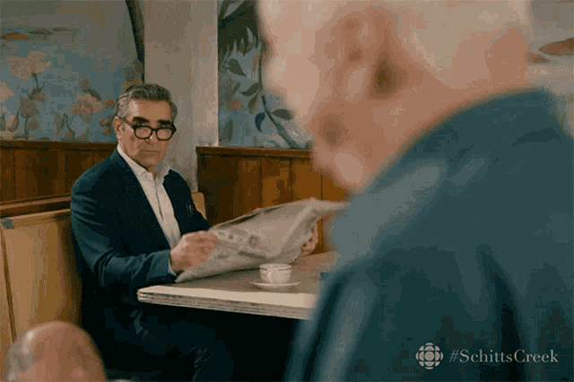 a man in a suit is reading a newspaper while sitting at a table with another man