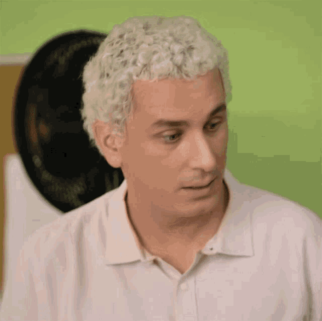 a man with white hair and a white shirt looks at the camera