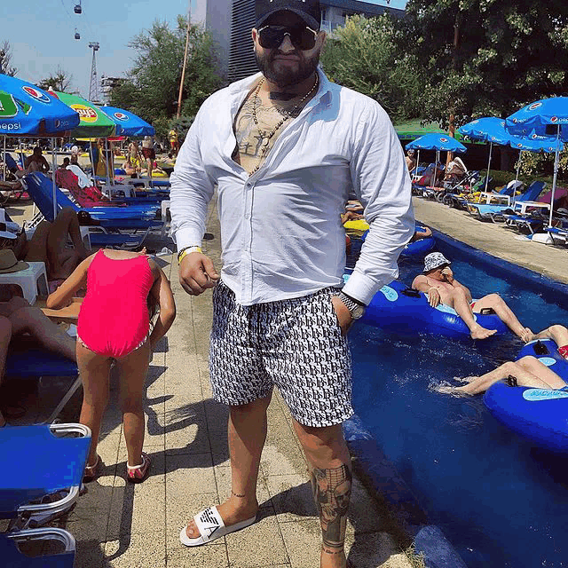 a man with a tattoo on his leg stands in front of a pool