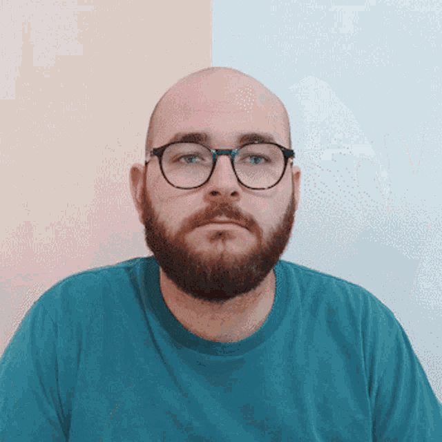a bald man with glasses and a beard wears a blue shirt