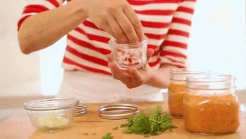 a woman in a red and white striped shirt is preparing food in jars .
