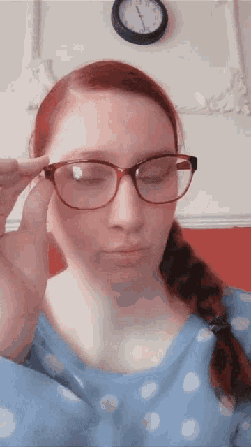 a woman adjusts her glasses in front of a clock that shows the time as 10:10