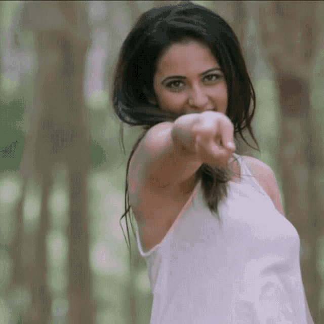 a woman in a white tank top is pointing at the camera with her finger .