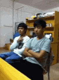 two boys are sitting in a room with their arms folded