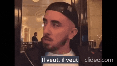 a man with a beard is wearing a black hat and says il veut il veut