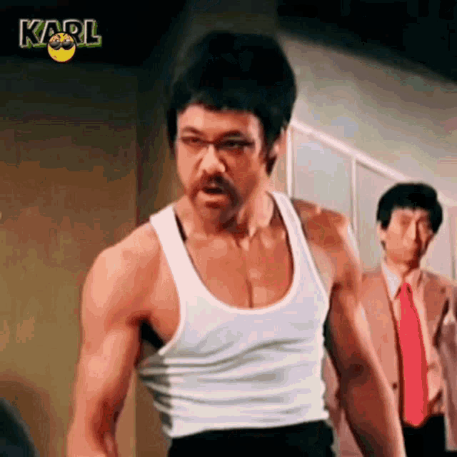 a man in a white tank top is standing in front of a man in a suit and tie .