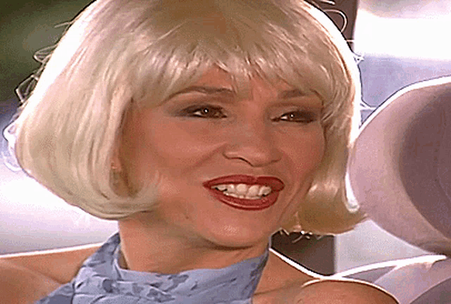 a woman wearing a wig and a blue scarf smiles for the camera