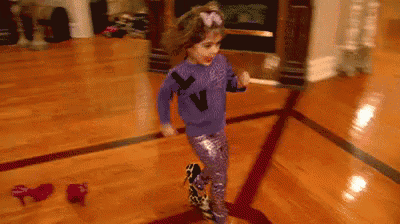 a little girl in a purple shirt is dancing on a wooden floor