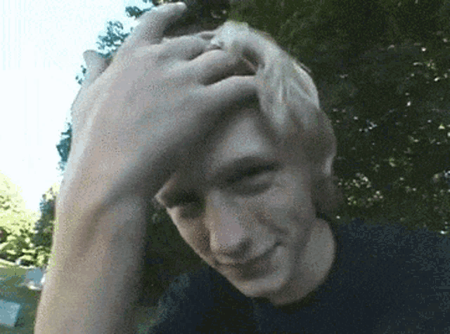a man scratches his head with his hand and smiles