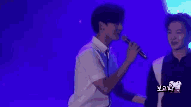 a couple of men standing next to each other on a stage with the words what on 2 cube on the bottom right
