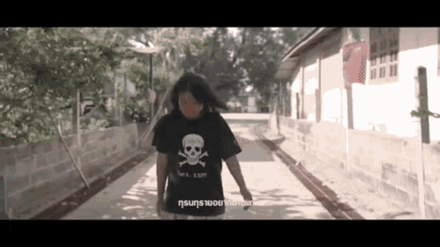 a woman wearing a black shirt with a skull and crossbones on it is walking down a street .