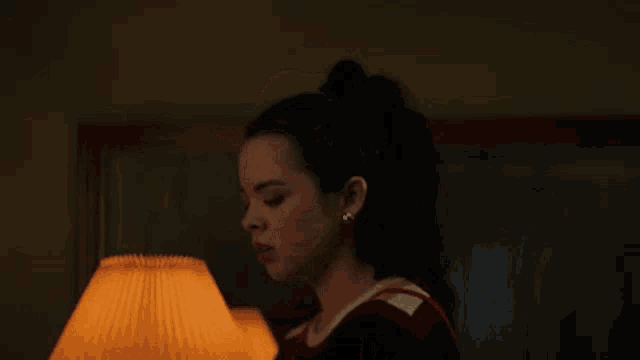 a woman in a red and black dress is standing in front of a lamp with her eyes closed .