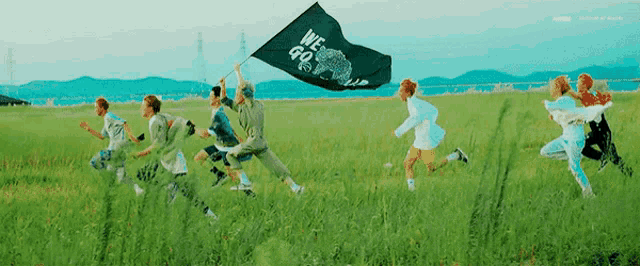 a group of people are running through a grassy field with a flag .