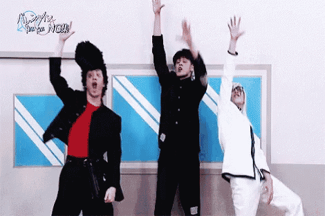a group of three men are standing next to each other with their arms in the air .