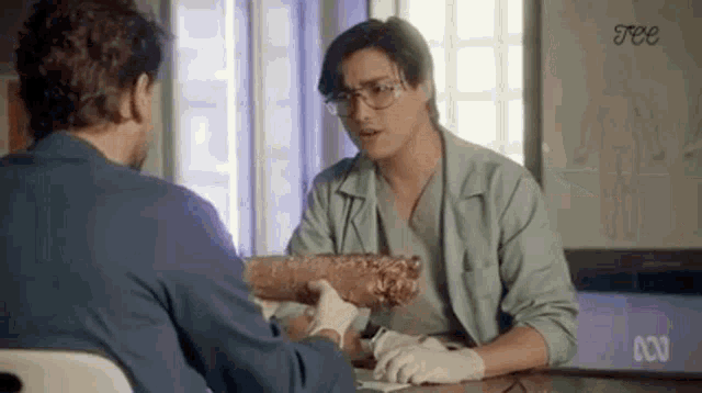 two men are sitting at a table talking to each other while one of them is holding a large piece of wood .