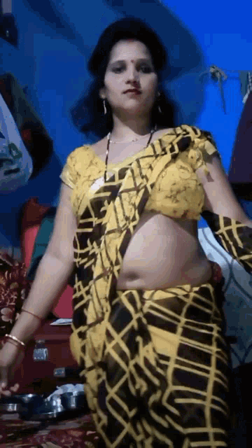 a woman in a yellow and black striped saree is standing on a bed .