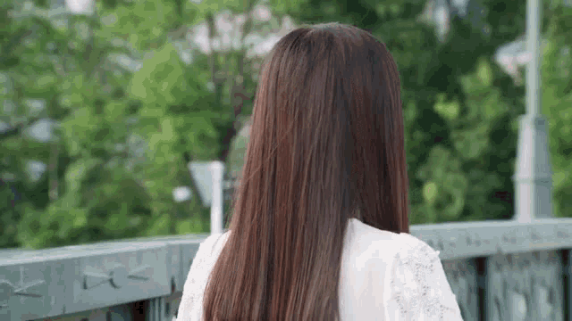 a woman with long brown hair is standing on a bridge .