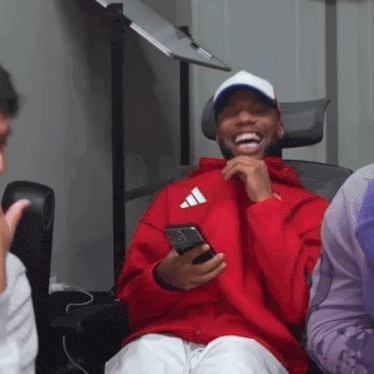 a man wearing a red adidas hoodie is laughing and holding a cell phone