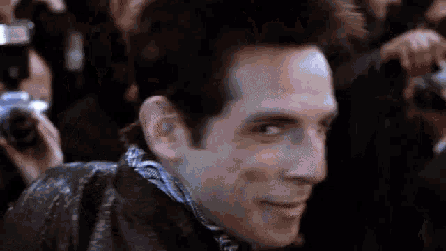 a man in a leather jacket is smiling in front of a crowd of people .